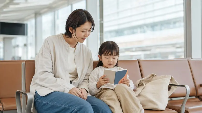 日本人の母親と幼い子どもが外出先で小さな絵本を読む様子