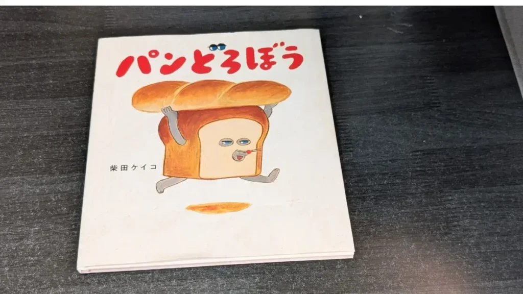 黒い机の上に置いた柴田ケイコ作の絵本『パンどろぼう』の表紙