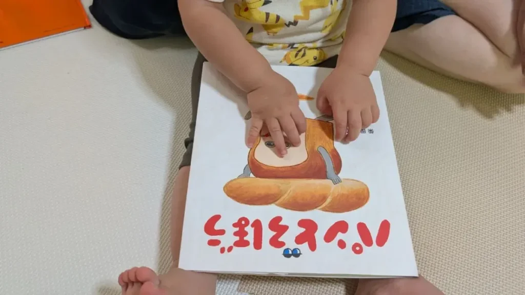 子どもが膝の上に絵本『パンどろぼう』を置き、両手で表紙に触れている様子