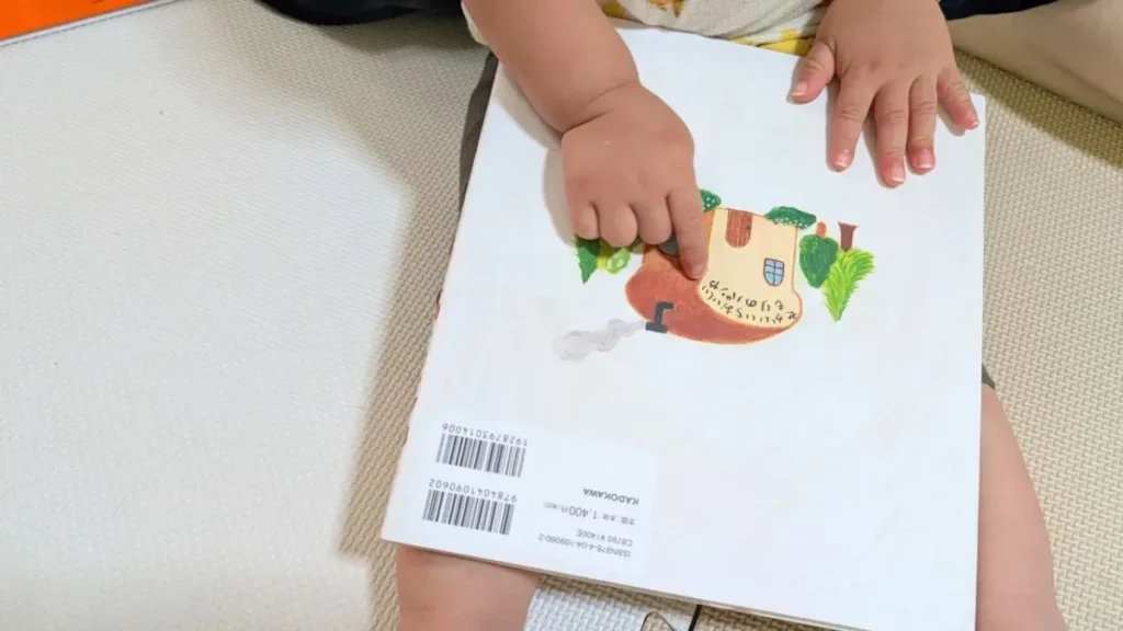 子どもが膝の上で絵本『パンどろぼう』の裏表紙を指さしている様子